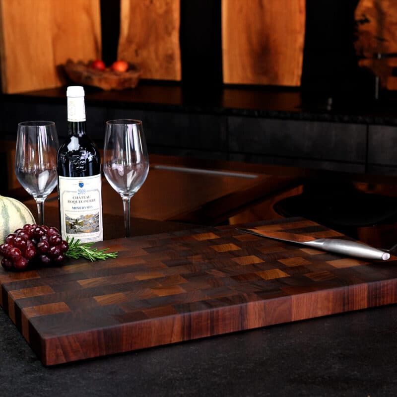 Stirnholz-Schneidebrett-Nussbaum in moderner Küche, hochwertige Messer und Weintrauben auf dem Brett, Weinflasche und Weingläser stehen daneben